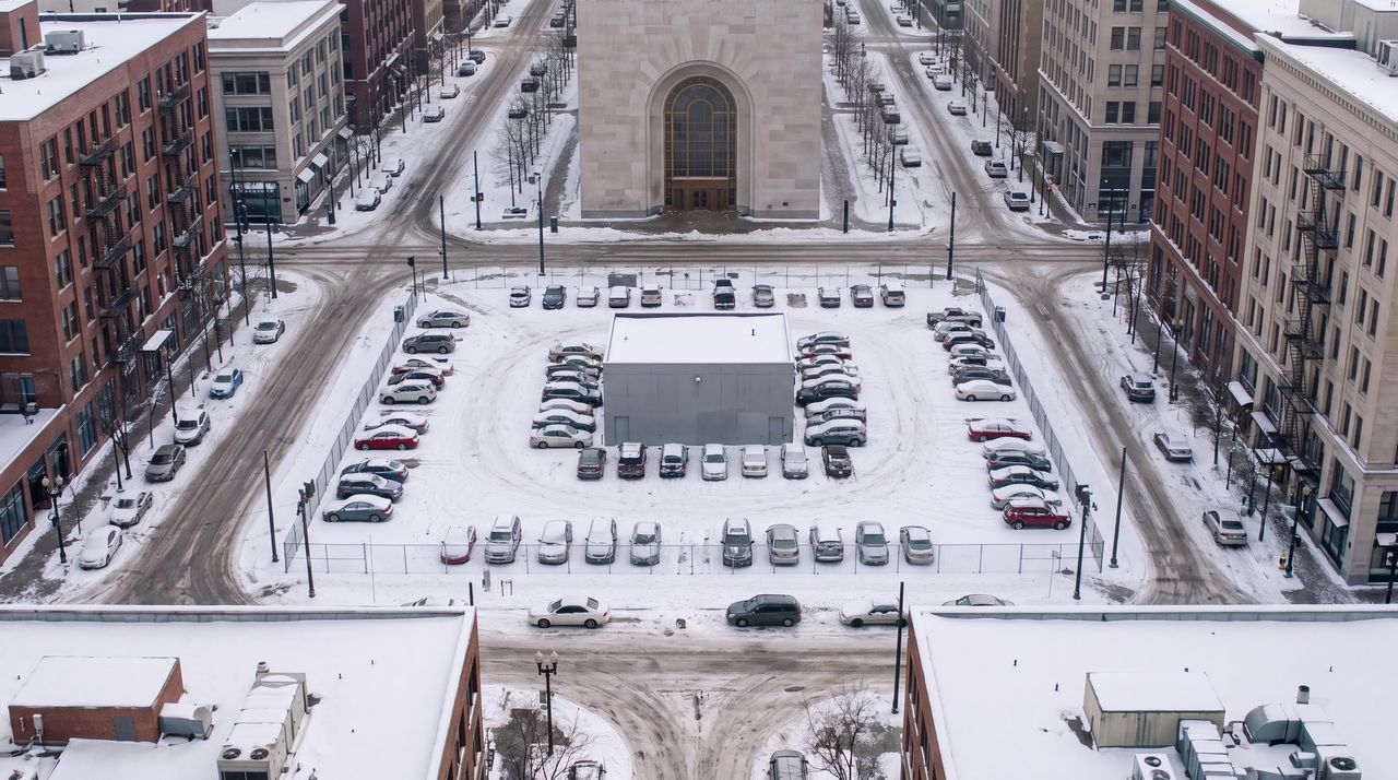 Today: The same square as it is now: a snow-covered parking lot full of cars, a plain gray utility building and a chain-link fence, under an overcast sky.