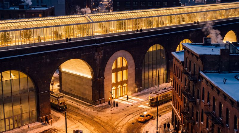 The Viaduct, after dark: The same street at night: the mile of glass along the viaduct glowing warm gold over the city, the arches lit from within, snow under the streetlights.
