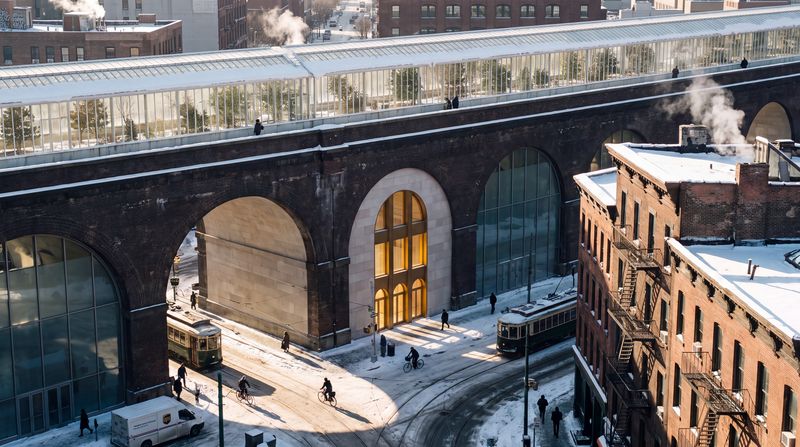 A street in a brick industrial district at noon in winter: a railway viaduct whose arches are filled with pale stone and warm glass, a long glasshouse promenade green with trees running along its top, people on a wide stair, and a tall gold doorway under the nearest arch.