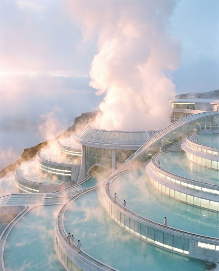 Terraced round pools of pale blue water on a white structure above the clouds, with a tall plume of steam and small figures walking the rims at dawn.